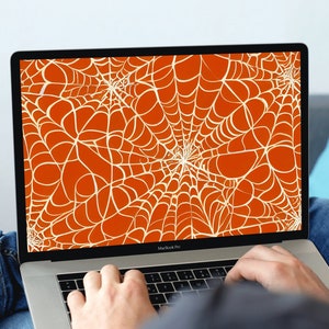 May include: A laptop computer with a bright orange and white spiderweb design on the screen. The laptop is open and the keyboard is visible. The person's hands are on the keyboard.
