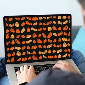 May include: A laptop computer with a black screen displaying a pattern of orange and yellow abstract shapes on a black background. The laptop is open and the keyboard is visible. The person's hands are typing on the keyboard.