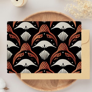 Puede incluir: Una tarjeta de felicitación con un patrón repetido de formas estilizadas en naranja y blanco sobre un fondo negro. La tarjeta está dentro de una bandeja de madera con un sobre beige.