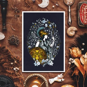 May include: A framed art print featuring a detailed illustration of a classical figure, possibly Athena, holding a spear and shield. The artwork is surrounded by floral and botanical elements, with a color palette of blues, golds, and whites. The print is set against a dark background.
