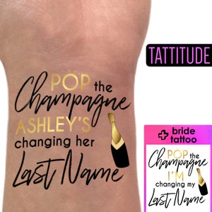 Könnte beinhalten: Goldenes und schwarzes temporäres Tattoo mit dem Text "Pop the Champagne Ashley's changing her Last Name" und einer Grafik einer Champagnerflasche.