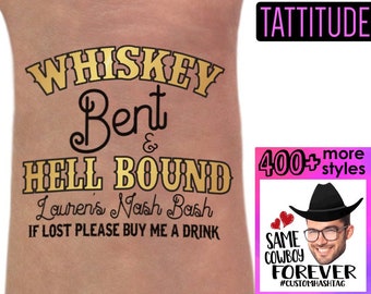 Op de afbeelding: Een gouden tijdelijke tatoeage met de tekst "Whiskey Bent & Hell Bound" en "Louren's Nash Bash" met de tekst "If Lost Please Buy Me A Drink" eronder. De tatoeage zit op de arm van een persoon. Een roze en wit bord met de tekst "TATTITUDE" zit in de rechterbovenhoek. Een roze en wit bord met de tekst "400+ more styles" zit in de rechterbenedenhoek. Een cartooncowboy met een hart en de tekst "Same Cowboy Forever #CUSTOMHASHTAG" zit in de rechterbenedenhoek.