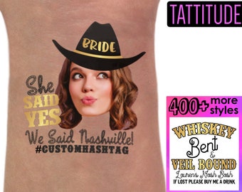 May include: A temporary tattoo with a bride wearing a cowboy hat and the text "She Said Yes We Said Nashville! #CUSTOMHASHTAG". The tattoo is on a person's arm. The image also includes a pink and black sign with the text "TATTITUDE 400+ more styles WHISKEY Bent & VEIL BOUND Lourer's Nash Bash IF LOST PLEASE BUY ME A DRINK".