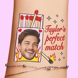 Könnte beinhalten: Ein temporäres Tattoo mit einer Streichholzschachtel-Illustration, in der ein lächelndes Gesicht zu sehen ist, umgeben von roten Herzen und gelben Flammen. Der Text "Taylor's perfect match" steht in roter Schrift neben der Schachtel.