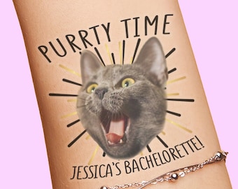 Puede incluir: Un tatuaje temporal con un gato gris de boca abierta, rodeado de líneas radiantes negras y doradas. El texto superior dice PURRTY TIME y el inferior JESSICA'S BACHELORETTE! El diseño está aplicado sobre la piel junto a una pulsera de cadena plateada.