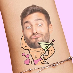 Image of a wrist with a custom face temporary tattoo adhered to it. The personalized face tattoo, often used for bachelorette parties or birthday party favors, features a cutout of a grooms face on a cartoon buff body that's flexing, holding a giant martini and wearing a bikini bottom. Design also features hearts and has space to add the grooms name as well.