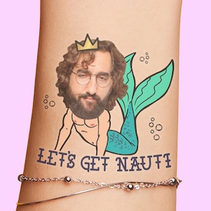 Op de afbeelding: Een tijdelijke tattoo met het gezicht van een bebaarde man met een bril, een gouden kroon en een turquoise zeemeerminstaart. De tekst "LET'S GET NAUTI" staat eronder. Een zilveren armband is zichtbaar.