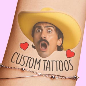 May include: A temporary tattoo featuring a person wearing a yellow cowboy hat with a surprised expression, two red heart icons, and the black text CUSTOM TATTOOS. The design is applied to skin and positioned above a thin silver chain bracelet.