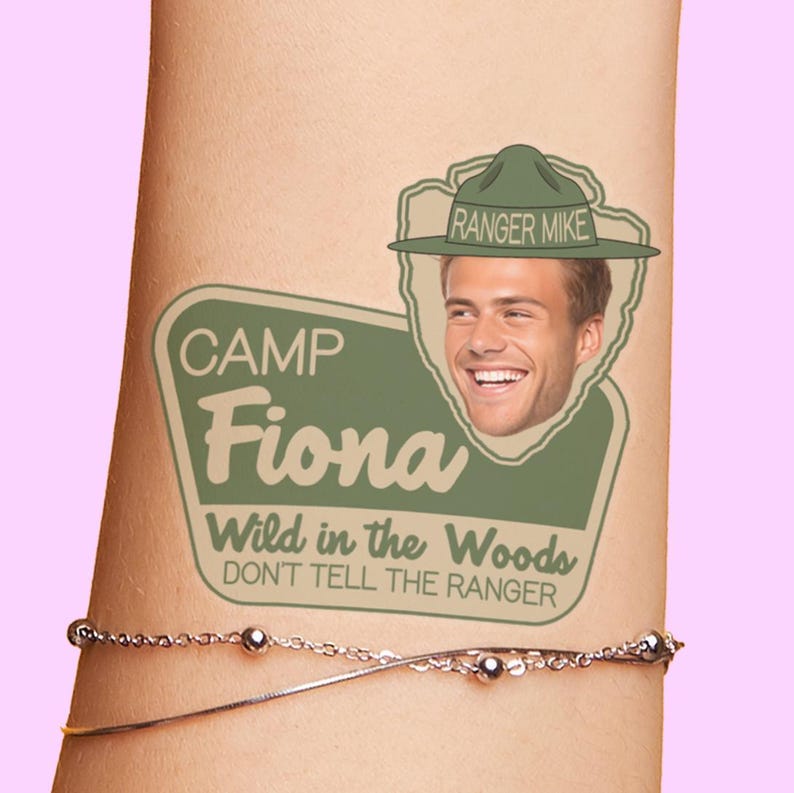 May include: A green and brown temporary tattoo with the text "Camp Fiona Wild in the Woods Don't Tell the Ranger" and a cartoon image of a man wearing a ranger hat. The text "Ranger Mike" is on the hat.