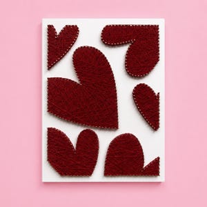 May include: A white rectangular board featuring six heart shapes created with dark red string wound around small metal nails. The string art design displays hearts of varying sizes and orientations arranged across the flat white surface.