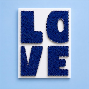 Peut inclure: Un panneau rectangulaire blanc présentant le mot LOVE réalisé en art du fil bleu foncé. Les lettres sont formées par des clous argentés enfoncés dans le panneau, avec du fil bleu tissé entre eux pour créer un aspect dense et texturé.