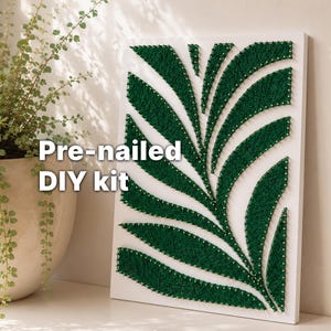 May include: A pre-nailed DIY kit featuring a white canvas with a green string art design of a leaf. The text "Pre-nailed DIY kit" is displayed on the left side of the canvas. The design is a modern, minimalist piece of wall art.
