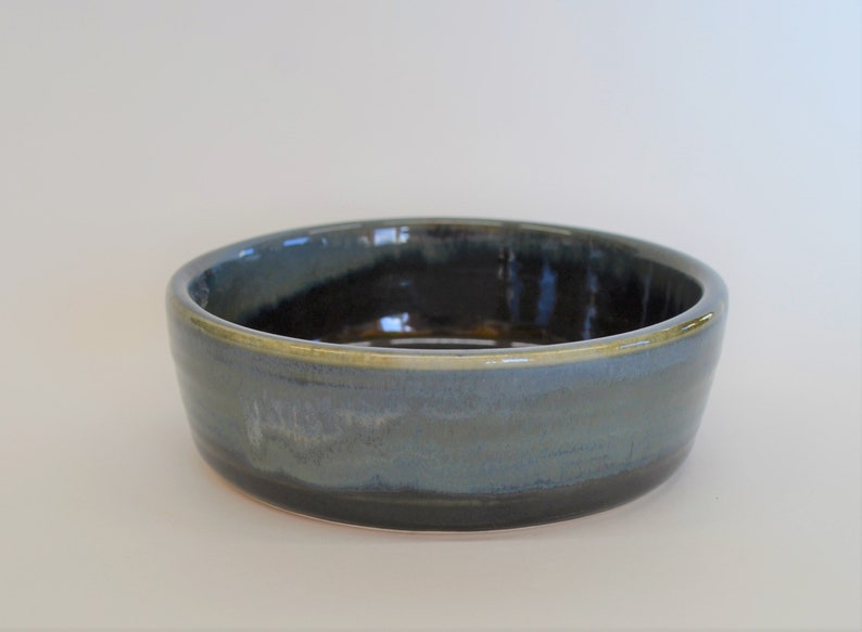 K&ouml;nnte beinhalten: Eine kleine, runde Keramiksch&uuml;ssel mit einer blauen und schwarzen Glasur. Die Sch&uuml;ssel hat einen leicht erh&ouml;hten Rand und eine glatte, gl&auml;nzende Oberfl&auml;che.