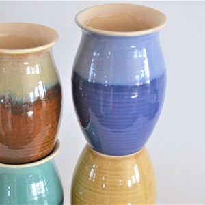 May include: Four ceramic vases stacked on top of each other. The top vase is light blue with a darker blue stripe. The second vase is brown with a light brown stripe. The third vase is a light green. The bottom vase is a light yellow.