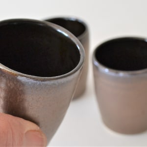 Peut inclure: Quatre tasses en céramique brun avec des intérieurs noirs. Les tasses ont un glaçage moucheté et une forme légèrement arrondie.