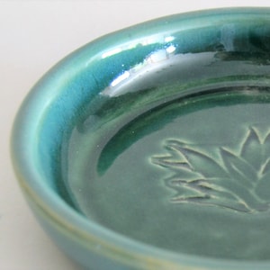 May include: A teal green ceramic dish with a raised design of a stylized agave plant.