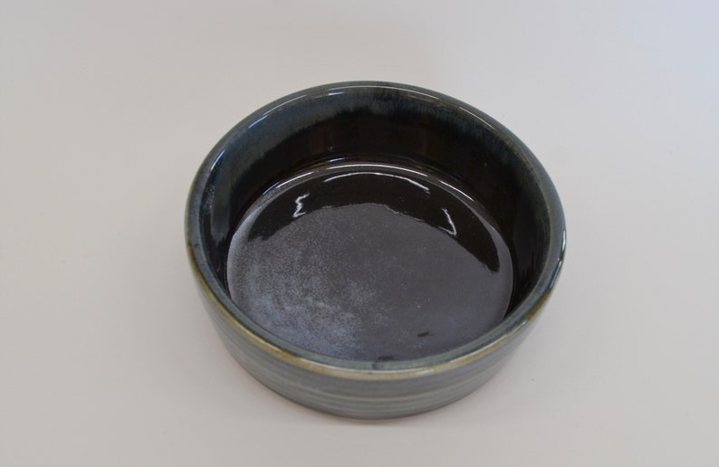 K&ouml;nnte beinhalten: Eine dunkelblaue Keramiksch&uuml;ssel mit hellblauem und gr&uuml;nem Glase. Die Sch&uuml;ssel hat einen glatten, abgerundeten Innenraum und einen leicht ausgestellten Rand.