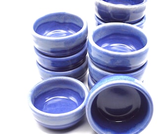 May include: A stack of ten small, blue and white ceramic bowls. The bowls are glazed with a light blue color and have a white rim.