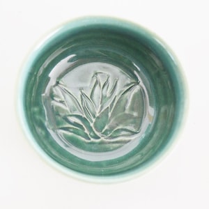 May include: A teal ceramic bowl with a raised floral design in the centre.