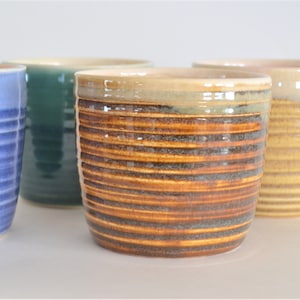 May include: Three ceramic mugs with striped patterns. The mugs are in shades of blue, green, and brown.