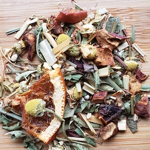 May include: A mix of dried herbs, fruits, and flowers for tea. The mix includes dried orange peel, apple pieces, chamomile flowers, and green leaves.