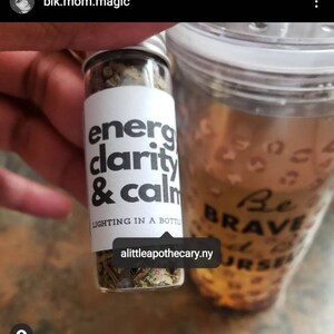 May include: A small glass jar filled with dried herbs and labeled "energy clarity & calm lighting in a bottle" with the website "alittleapothecary.ny" printed on the label.