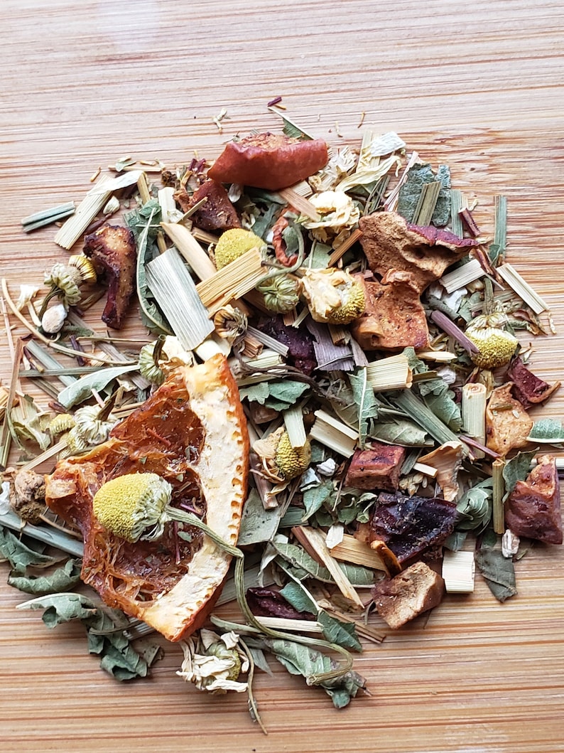 May include: A mix of dried herbs, fruits, and flowers for tea. The mix includes dried orange peel, apple pieces, chamomile flowers, and green leaves.