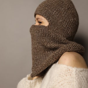 Puede incluir: Una balaclava de punto marr&oacute;n con una solapa abatible que cubre la cara. La balaclava se lleva sobre un su&eacute;ter de punto blanco.