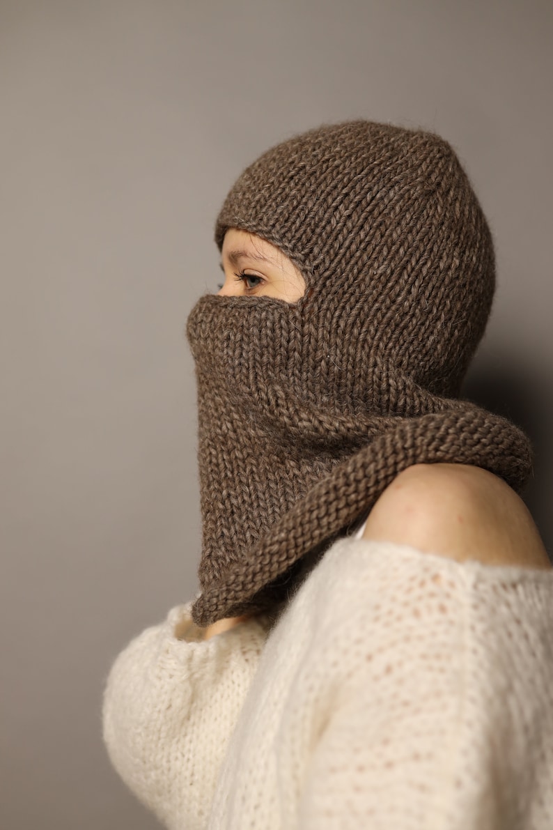 Puede incluir: Una balaclava de punto marr&oacute;n con una solapa abatible que cubre la cara. La balaclava se lleva sobre un su&eacute;ter de punto blanco.