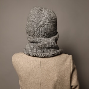 Puede incluir: Un conjunto de gorro y bufanda de punto gris. El gorro es de estilo beanie holgado y la bufanda es de estilo cuello de tortuga.