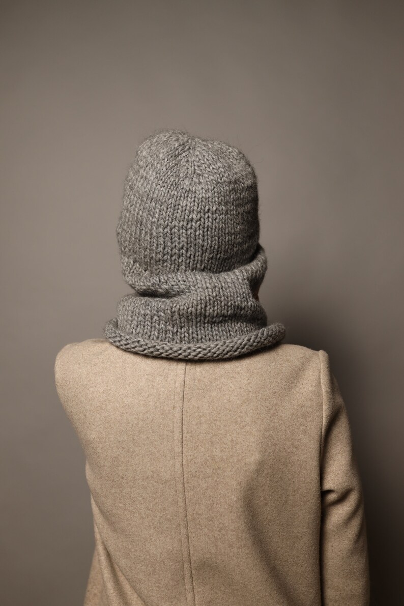 Puede incluir: Un conjunto de gorro y bufanda de punto gris. El gorro es de estilo beanie holgado y la bufanda es de estilo cuello de tortuga.