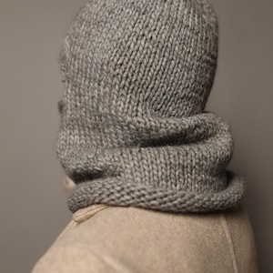 Puede incluir: Una bufanda de punto gris con capucha y una textura gruesa y de punto grueso. La bufanda est&aacute; doblada hacia abajo para crear un cuello de tortuga.