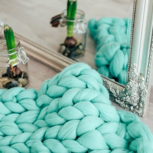 May include: A turquoise chunky knit throw blanket with a silver ornate mirror in the background.
