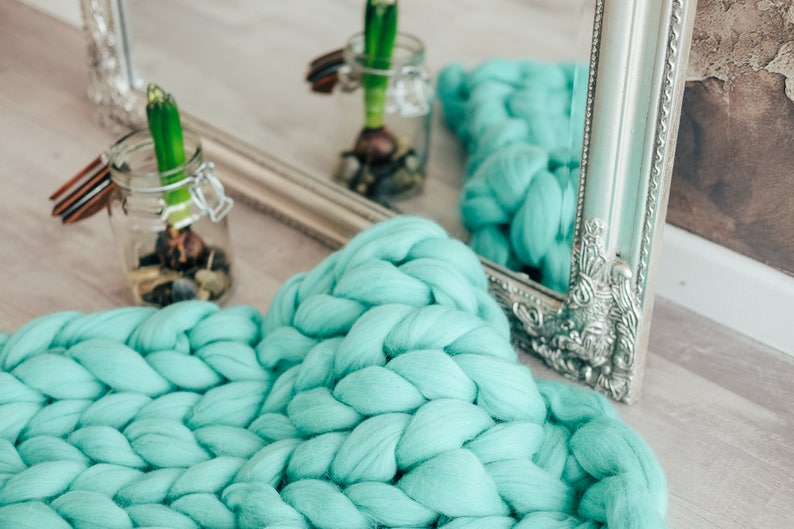 May include: A turquoise chunky knit throw blanket with a silver ornate mirror in the background.
