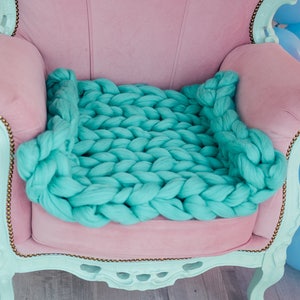 May include: A light pink armchair with a large, chunky knit turquoise blanket draped over the seat.