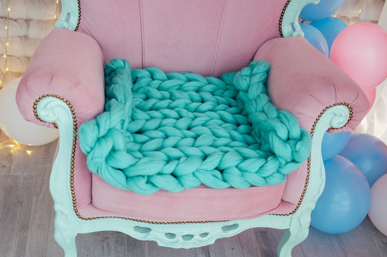 May include: A light pink armchair with a large, chunky knit turquoise blanket draped over the seat.