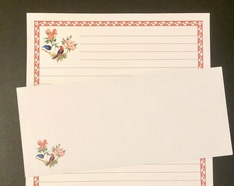 May include: A white lined stationery set with a red border and a floral design featuring pink roses and blue birds. The stationery set includes a sheet of paper and an envelope.