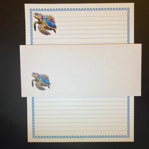 May include: A set of three stationery note cards with a blue and white border and a colorful sea turtle illustration. The cards are blank inside for writing.