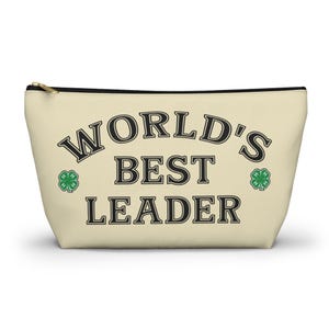 Peut inclure: Pochette zippée de couleur crème avec l'inscription "WORLD'S BEST LEADER" en noir, avec des motifs de trèfles à quatre feuilles verts de chaque côté. La pochette a une fermeture éclair noire et un curseur doré.