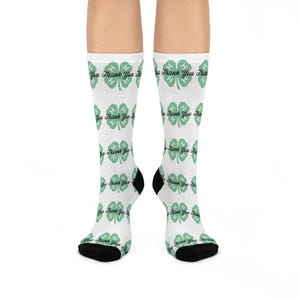 May include: White socks with a repeating pattern of green four-leaf clovers and the words "Thank You". The socks have black heels and toes. The socks are a fun accessory.