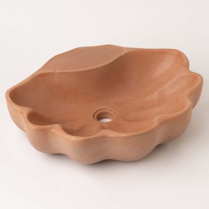 May include: A terracotta-colored ceramic sink with a wavy, organic shape and a single drain hole in the center.