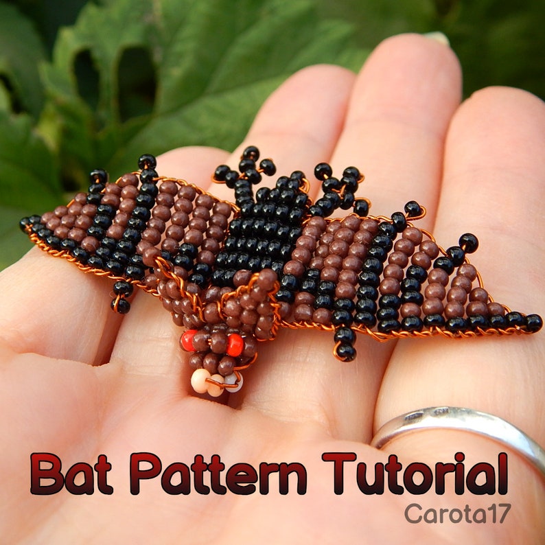 May include: A brown and black beaded bat with red eyes, made with wire and beads. The bat is held in a hand. Bat Pattern Tutorial Carota17