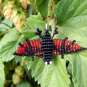 May include: A beaded bat charm with black and red beads. The bat is hanging from a green leaf.