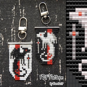 May include: Two beaded keychains with a shield design. One keychain features a black and red design, while the other has a white and red design. Both keychains have a silver-colored metal clasp. The text "PDF Pattern by Carola17" is visible.