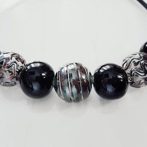 May include: A black elastic bracelet with six beads. Two of the beads are black, two are silver with a swirl pattern, and two are silver with a striped pattern.