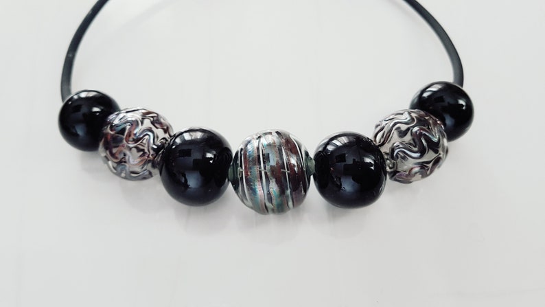 May include: A black elastic bracelet with six beads. Two of the beads are black, two are silver with a swirl pattern, and two are silver with a striped pattern.
