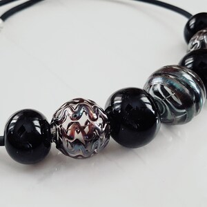 May include: A black elastic necklace with six beads. The beads are black, silver, and clear with a swirling pattern.