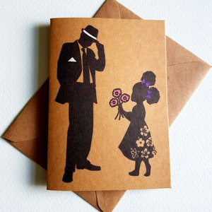 Könnte beinhalten: Eine braune Grußkarte mit einer schwarzen Silhouette einer Person in Anzug und Hut und einem Kind, das Blumen anbietet. Das Kleid des Kindes hat florale Muster. Die Karte wird von einem braunen Umschlag begleitet.