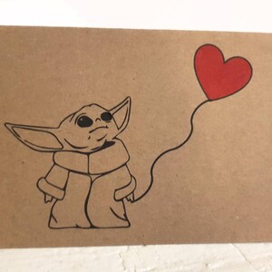 May include: A brown card with a black and white illustration of a character from the Star Wars franchise, holding a red heart-shaped balloon.