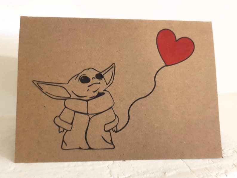 May include: A brown card with a black and white illustration of a character from the Star Wars franchise, holding a red heart-shaped balloon.